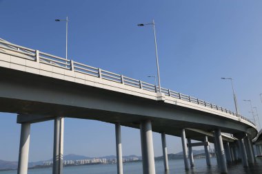 Bir köprü, üzerinde açık mavi bir gökyüzü olan bir su kütlesini kaplar. Köprü uzun ve uzundur, uzunluğu boyunca birkaç ışık görünür. Sahne sakin ve sakin, aşağıdaki suyla