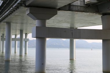 Arka planda dağ olan bir su kütlesinin üzerinde bir köprü. Köprü boş ve su sakin.