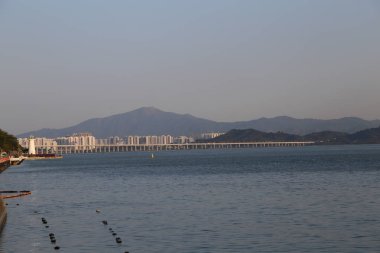 Köprü, arka planda bir dağ bulunan bir su kütlesini kapsar. Gökyüzü açık ve su sakin.