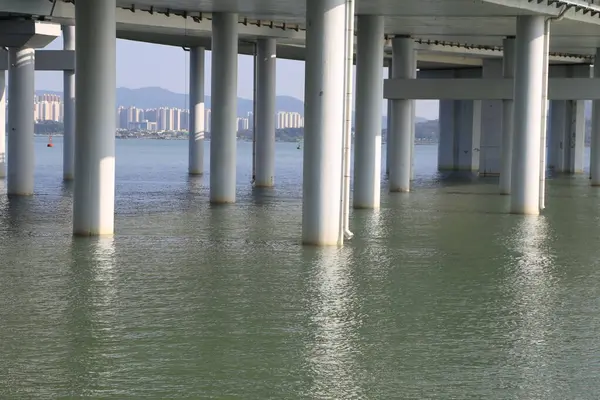 Arka planda bir şehir olan bir su kütlesinin üzerinde bir köprü. Su sakin ve köprü boş.