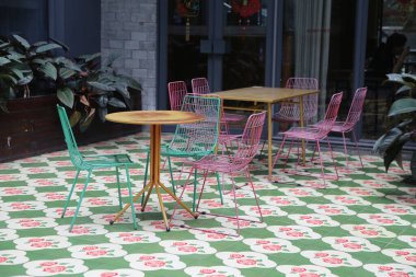 Yeşil ve pembe fayanslı, çeşitli sandalye ve masaları olan renkli bir bahçe. Sandalyeler misafirperver ve davetkar bir ortam yaratacak şekilde dizildi.