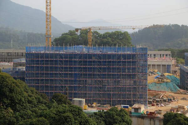A construction site with a large building in the background. The building is being built with scaffolding and is surrounded by trees