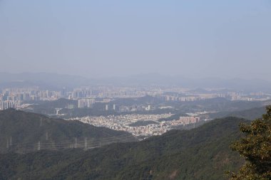 Shenzhen 'de her iki tarafında yüksek binalar ve yeşil dağlar olan bir kentsel alan vardır. Önlerinde orman kaplı tepeler, altlarında da başka bir şehir vardır. Gökyüzü bulutsuz, berrak görünüyor..