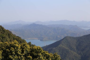 Dağ sırasının manzarası, her iki tarafında sarı çiçekler açan ve önünde bir göl, çok geniştir, dağlarla çevrilidir, ve açık bir gökyüzü olmalıdır. Uzakta, birkaç tepe görülebilir..