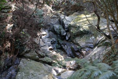 Küçük şelale ve kayalarla çevrili, yukarıdan çekilmiş kayalık bir arazinin fotoğrafı. Kamera yere doğru bakıyor.