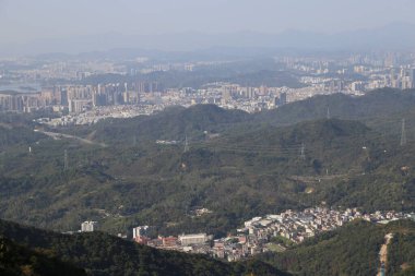 Uzakta, Shenzhen 'in kuzey dağlık bölgesinde yeşil bitki örtüsüyle kaplı bazı yüksek binalar ve alçak tepeler görebilirsiniz. Önünde başka bir yamaç daha var. Orada birçok ev vardı..
