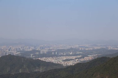 Uzakta, Shenzhen 'in ufuk çizgisini ve dağ manzarasını yüksek irtifadan görebilirsiniz. Önünde yeşil dağlar bulunan uzak manzara uçsuz bucaksızdır. Yakın mesafede, küçük tepelerin her iki tarafında da binalar vardı.