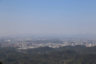 Uzakta, Shenzhen 'de yüksek irtifadan görülebilen binaları olan bir kentsel alan vardır. Önünde yeşil dağlar ve ormanlarla kaplı yamaçlar uzanır..