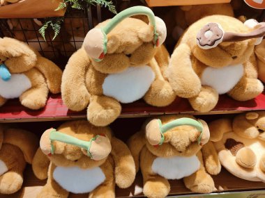 Mağazadaki raflarda sergilenen birkaç pelüş ayının kulaklıklı fotoğrafı. Kulaklar ve saç bantları kahverengi kürklerini tamamlamak için yumuşak yeşil süslemeler içerir..