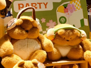 Arkaplanda yeşil ve sarı kareli kağıtlarla raflarda oturan sevimli, sevimli bir çift oyuncak ayı. Kulaklarının etrafında beyaz kulaklıklar var. Doldurulmuş hayvanlar birlikte otururken mutlu ve rahat görünüyorlar.