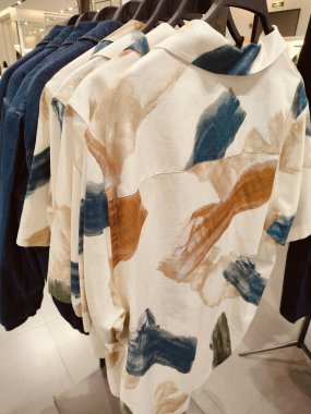 Üzerinde mavi ve yeşil desenler olan bir dizi gömlek. Gömlekler askıda asılı.