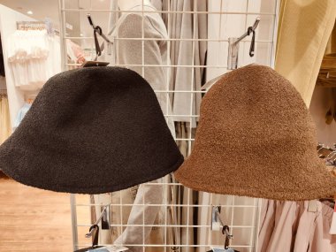 Mağazadaki açık bir askıda sergilenen yün ve saç telinden yapılmış iki farklı kova şapka. İlk şapka siyah, geniş kenarlı ve çene seviyesinin hemen altına düşüyor..