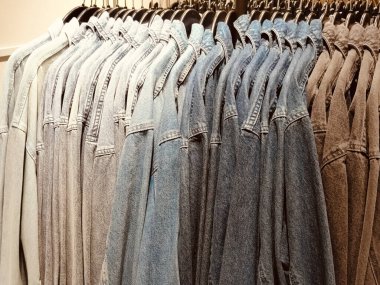 Her biri farklı renk ve tarzlara sahip bir sıra kot ve gömlek askıda asılı. Gömlekler gri renktedir, bütün kotlar soluk mavi renktedir. Arka planda bir mağaza ayarları görülebilir.