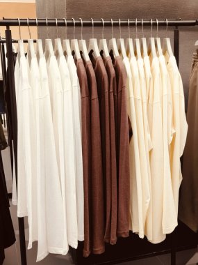 Mağazada bej renkli, minimalist tarzda, yüksek çözünürlüklü, yüksek kaliteli ve yüksek detay içeren beyaz ve kahverengi tişörtler var.