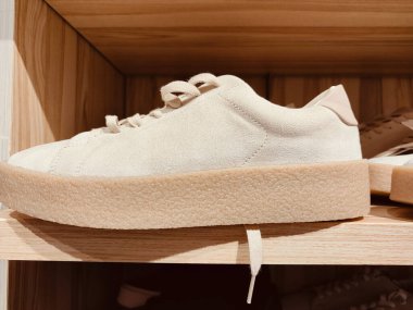 Mağazada ahşap tabanlı bir çift beyaz spor ayakkabı, yumuşak krem rengi, düşük üst tasarım, çok detaylı özellikleri ve açık bej ve açık kahverengi renklerin kombinasyonu