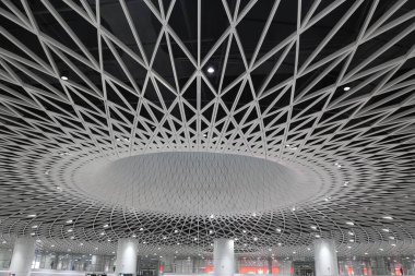 Shenzhen 'deki yüksek hızlı tren istasyonunun tavanında, üzerinde karmaşık bir ağ yapısı oluşturan beyaz metal kirişler oluşturan ayrıntılı bir geometrik desen bulunur..