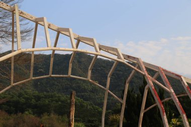 Gerçek fotoğraflarda farklı açılardan görülebilen, dağda kemerli şekilli beyaz metal bir yapı inşa ediliyor. Sahnede yeşil ağaçlar ve mavi bir gökyüzü var..