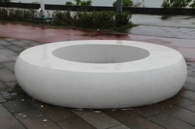 Yuvarlak bir tabanı ve düz bir yüzeyi olan bir açık hava parkının zemininde beyaz beton bir halka bulunur. Dairesel bir şekli var..