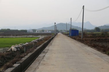 Çin 'in kırsal bölgelerinde asfalt beton yüzeyi ve alçak duvarları olan bir yol. Yeşil pirinç tarlaları onların yanında görülebilir.