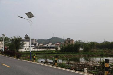Çin 'in kırsal kesimindeki güneş ışığı çok alçaktır ve onun yanında evler olmalı. Yanında eski bir nehir var. Yakınlardaki yol yüzeyinde her iki tarafta da yeşil bitkiler var..
