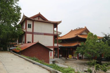 Kırmızı tuğlalı duvarları ve beyaz duvar panelleri olan iki katlı bir bina. Önünde ana salonun dış perspektifi var. Sol taraf ahşap saçaklar ve çatı kiremitleri olan tek katlı modernist bir ev.