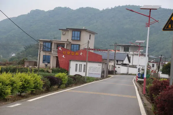 Üzerinde güneş panelleri olan dış duvar, beyaz duvarlar ve kırmızı fayanslar, Çin kırsalında iki katlı binalar, yeşil dağlarla çevrili, çevresindeki yollar, yol kenarındaki sarı çizgiler, yol kenarındaki sokak ışıkları, bu caddeler boyunca dikilen çiçekler,