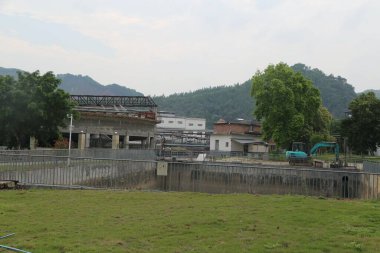 Büyük yeşil makineli bir inşaat alanı. Makine çukur kazıyor. İnşaat alanının etrafında çit var.