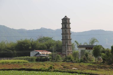 Güney Çin 'in kırsalında yeşil tarlaların ve dağların önünde antik bir taş kule var. Manzaraya göre bir tarafında eğimli çatıları olan iki küçük ev var.