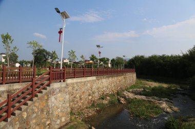 Demir tırabzanlı kırmızı taş bir köprü nehir kıyısına çıkıyor. Bir tarafında bir güneş ışığı direği ve altında insanların ayakta durabildiği ya da yürüyebildiği diğer ışıklar vardır..