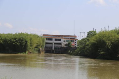 Nehrin arka planında büyük bir bina var. Bina beyaz ve turuncu. Su kahverengi ve bulanık.