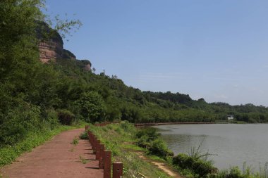 Kırmızı toprak yol nehir boyunca uzanır, her iki tarafında yeşil bitki örtüsü ve önünde kayalıklar vardır. Uçurum ağaçlarla kaplı. Ayağında eski bir tapınak binası var..