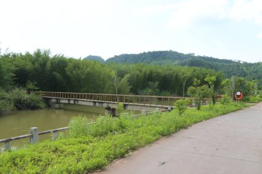 Nehir boyunca uzanan köprü, her iki tarafında yeşil bitki örtüsü ve ağaçlarla çevrili asfalt bir yol boyunca inşa edilmiştir. Patikanın kenarı başka bir tahta korkuluğa çıkıyor.
