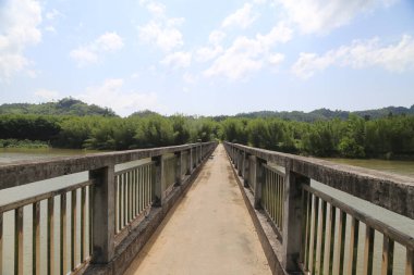 Nehrin üzerindeki köprü betondan yapılmıştır ve her iki tarafında bariyerler ve arkasında mavi bir gökyüzünün altında yeşil ağaçlar vardır. Önünüzdeki yol yüzeyi diğer tarafa doğru uzanır, yürümek ve bisiklete binmek için açık bir alan yaratır.