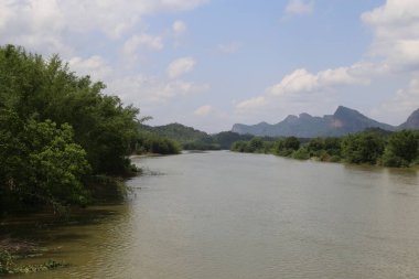 Güney Çin 'de bir nehir, her iki tarafında yeşil bitki örtüsü ve arkasında dağlar var. Su sakin, yukarıdaki mavi gökyüzünü yansıtıyor..