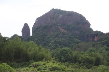 Uzakta büyük bir dağ, yoğun yeşil ağaçlar ve keskin tepeleri olan kırmızı kayalarla çevrili. Kaya eski bir ejderha kafası şeklinde..