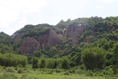 Uzakta yeşil bitki örtüsü ve her iki taraftaki bambu ormanlarıyla çevrili büyük kırmızı kumtaşı bir dağ. Kayaların farklı şekilleri var, bazıları pürüzsüz, bazıları ise çatlak ve oyuklara sahip. Bu onlara eski bir his veriyor.