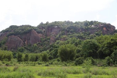 Arka planda yeşil bitki örtüsü ve düz zeminde bambu ormanlarıyla çevrili kırmızı kumtaşı bir dağ. Resim, üssün bir fersah uzağından çekildi. Detayları yakalamak için.