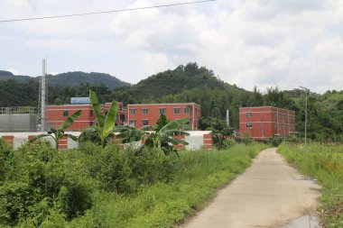 Çin 'in kırsal kesiminin ortasında kırmızı tuğlalı binalar ve beyaz duvarlarla çevrili bir sanayi parkı var. Her iki tarafta yemyeşil bitkiler vardı..