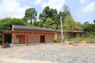 Güney Çin 'in kırsal kesimlerinde, düz çatılı ve ahşap pencereli eski bir kırmızı tuğla ev var. Önünde, koyu gri tuğlalardan yapılmış, ahşap kapılı ve zeminli iki basit, modern tuvalet duruyor..