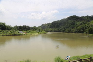 Parkın her iki tarafında yeşil bitki örtüsü ve çayırlarla çevrili büyük bir göl. Su yüzeyi sakin ve içinde yüzen küçük tekneler var..