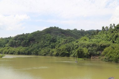 Uzaktaki yeşil dağ yoğun bambu ormanlarıyla çevrilidir ve her iki tarafında koyu kahverengi çalılar ve kır çiçekleriyle kaplı yüksek tepeler bulunur. Aşağıdaki geniş nehir aralarından yavaşça akıyor.