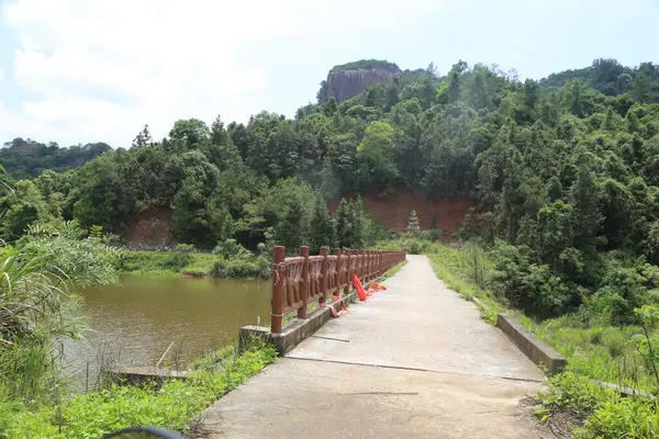 Kırmızı ve turuncu barikatları olan bir nehir üzerinde köprü. Köprü tahtadan yapılmıştır ve bir ormanda yer almaktadır.