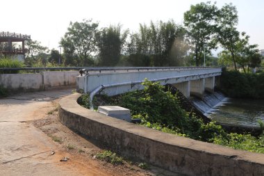 Bir beton köprü, yanında boru ağı ve borular bulunan bir sanayi parkının önündeki nehri kapsar. Fotoğraf yakınlardaki bir yoldan çekilmiş..