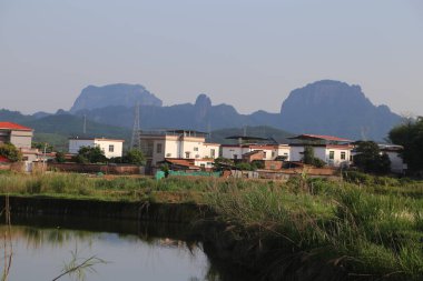 Güney Çin 'de küçük bir köy, dağlık bölgede yeşil otlaklarla çevrili beyaz evleri ve kırmızı çatıları var. Önünde kırsal kesimde akan eski bir nehir var..