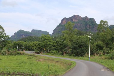Yol dağ zirvesine çıkar, her iki tarafında yeşil ağaçlar ve çimenler vardır. Uzak manzara, yoğun ormanlarla kaplı iki yüksek dağın önünde eski kırmızı bir uçurum olduğunu gösteriyor..
