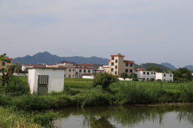 Uzakta, nehrin kıyısındaki birkaç küçük binanın bir tarafında beyaz duvarlar ve kırmızı fayanslarla izole edilmiş bir kırsal alan var. Önünde yeşil otlaklarla çevrili iki tane üç katlı modern ev duruyor..