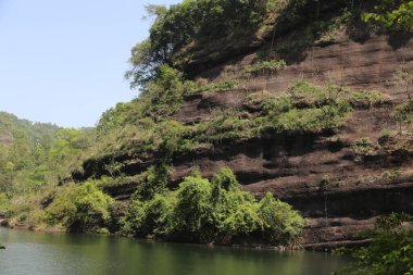 Zümrüt yeşili bir gölün kenarındaki uçurum, yemyeşil bitki örtüsü ve duvarlarının içinden uzanan dev ellere benzeyen siyah kaya oluşumlarıyla kaplıdır. Uçurumlar çok eski ve heybetliydi mavi gökyüzünün arka planına karşı.