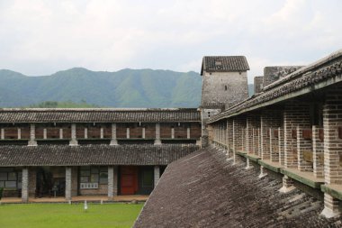 Eski askeri üssün tuğla duvarı, üstünde yüksek bir platform ve kırmızı tuğlalar var. Duvarların önünde yeşil çimenler varken koyu gri fayanslar vardır..