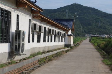 Siyah pencereli ve klimalı beyaz duvarlar yavaşça sağa uzanıyor, ki bu Çin 'in kırsal kesiminde bir açık hava sahnesi. Her iki tarafta yeşil bitki örtüsü var, uzak dağlara doğru gidiyor..