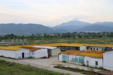Çin 'in kırsal kesimindeki pirinç tarlaları ve dağlarla çevrili sarı çatılı depo kompleksinin manzarası. Çatı beyaz beton duvarlarla kaplı..